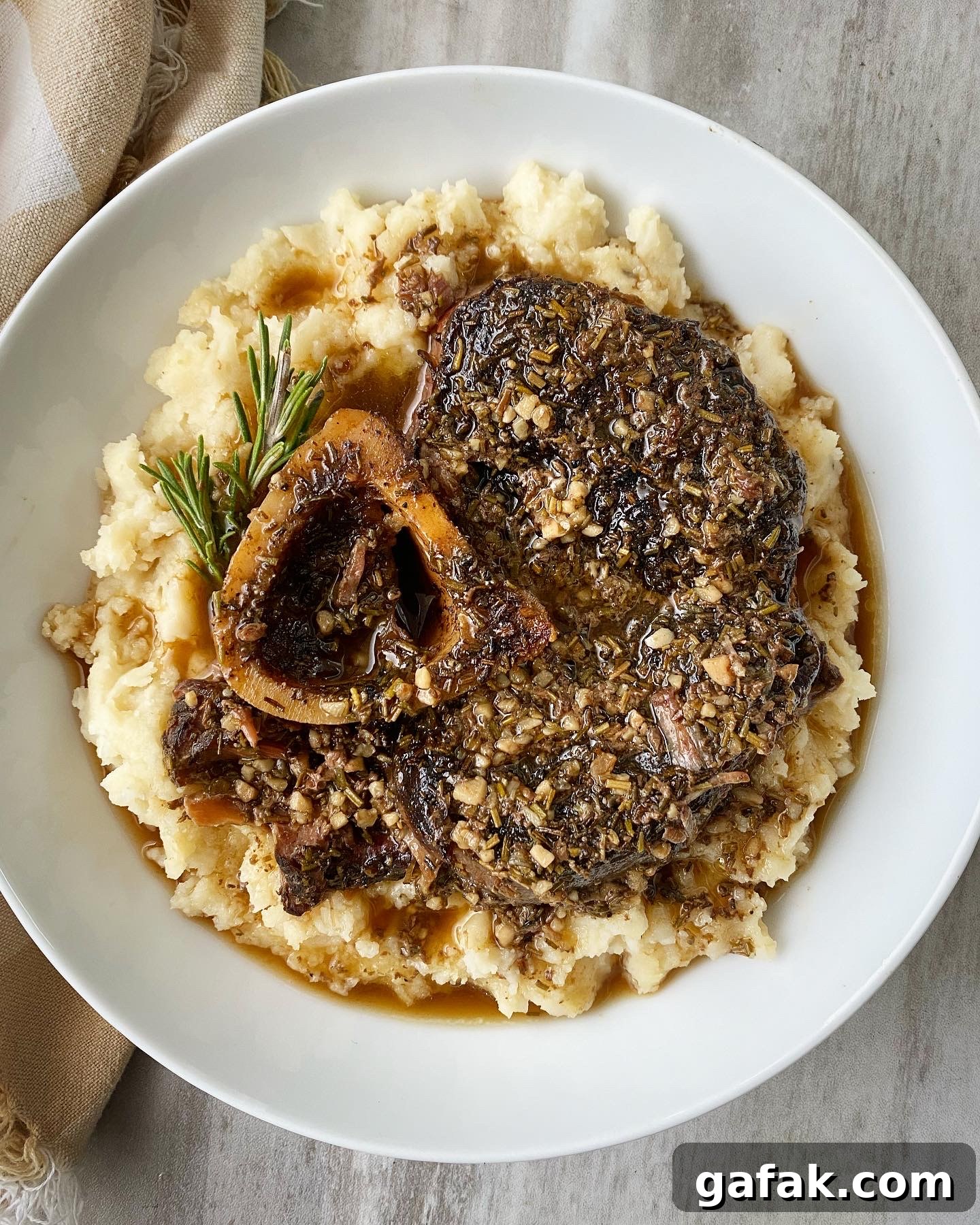 overhead shot of garlic herb beef shanks served over mashed cauliflower in a white bowl