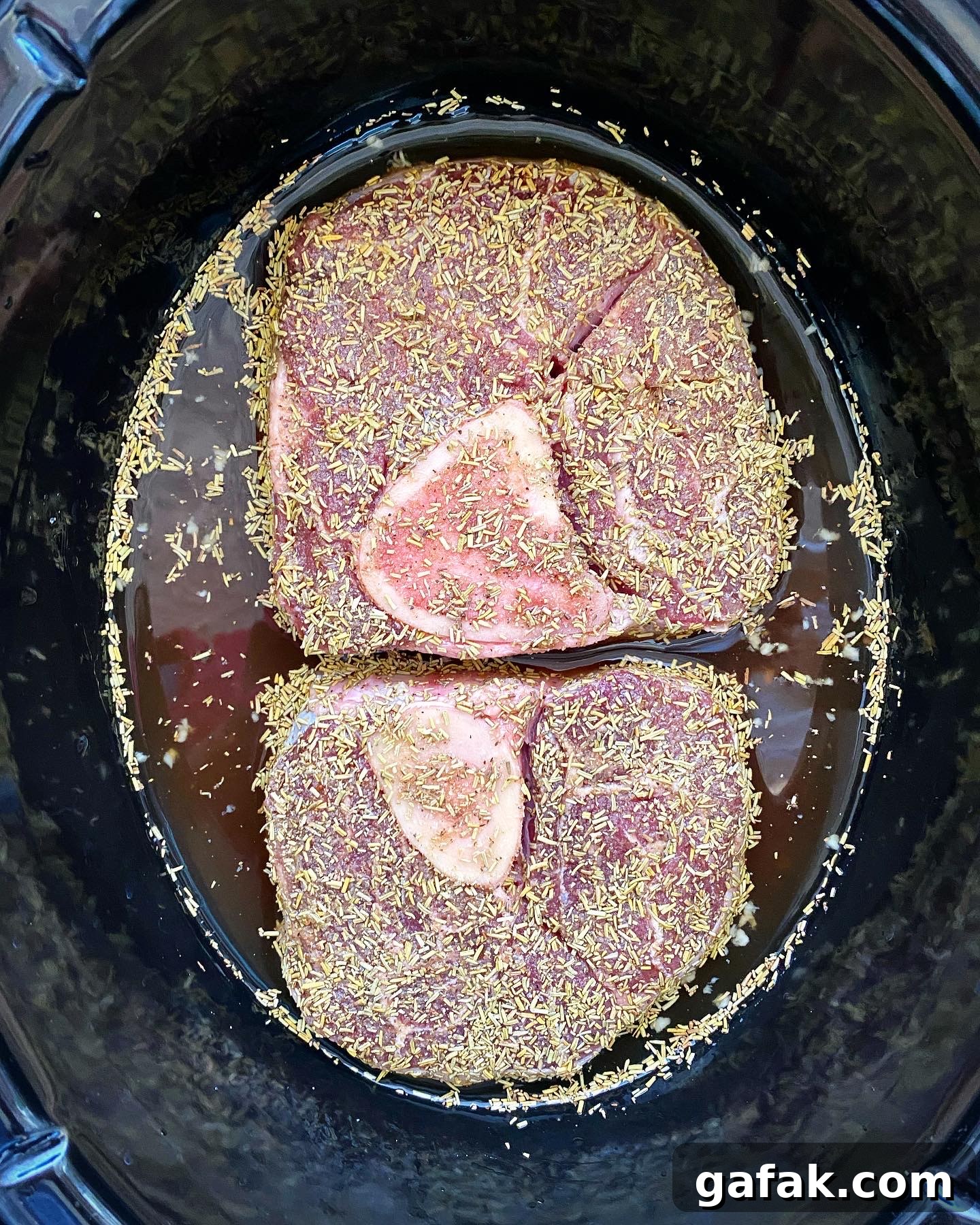 overhead shot of seasoned, uncooked beef shanks in a black crockpot