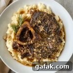 overhead shot of garlic herb beef shanks served over mashed cauliflower in a white bowl