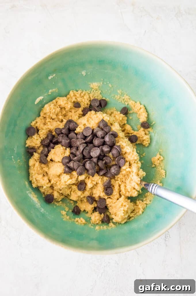 A bowl with raw chocolate chip cookie dough in it with a spoon in it.