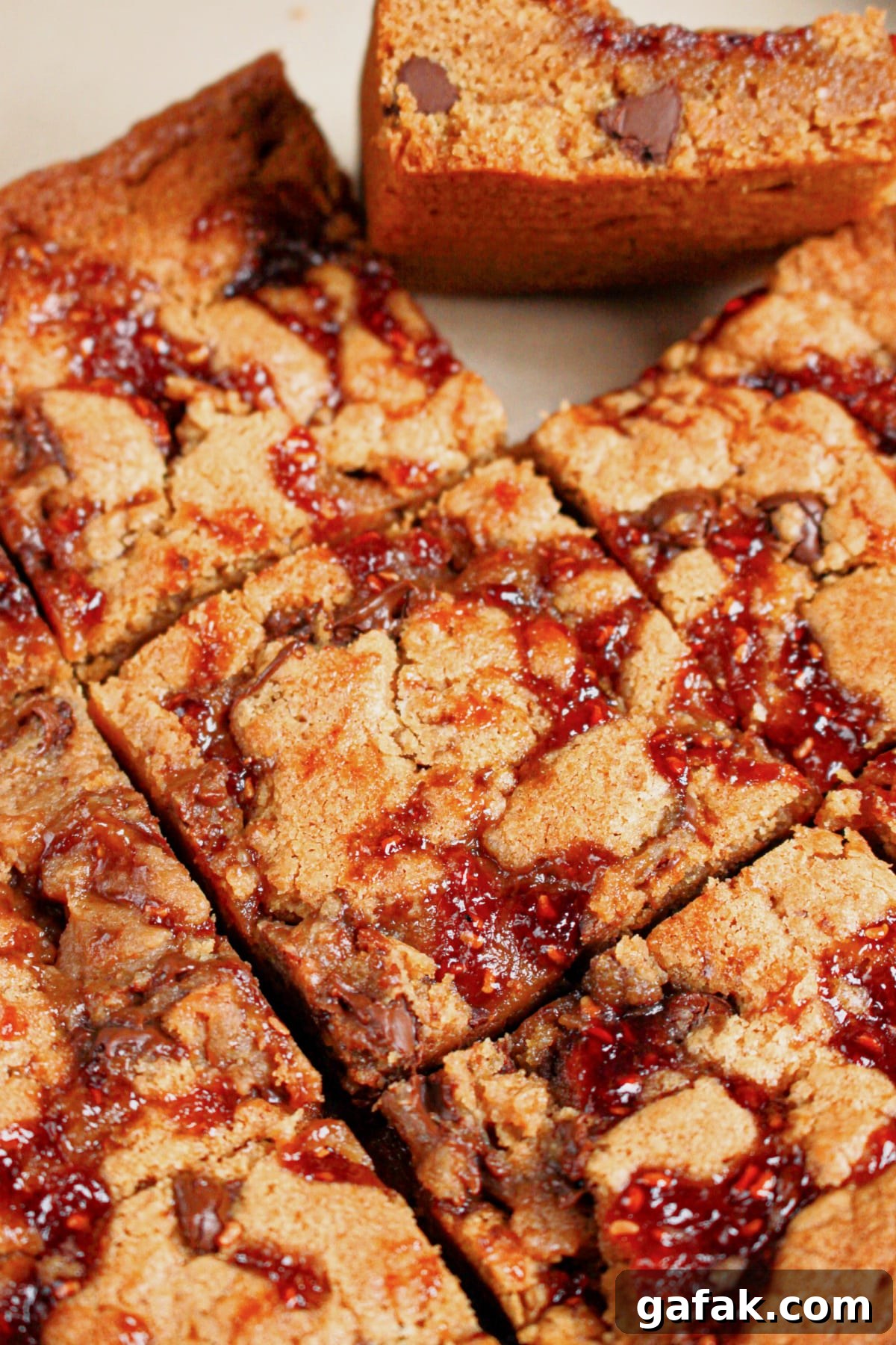 Peanut butter chocolate chip brownies topped with jam cut into squares.