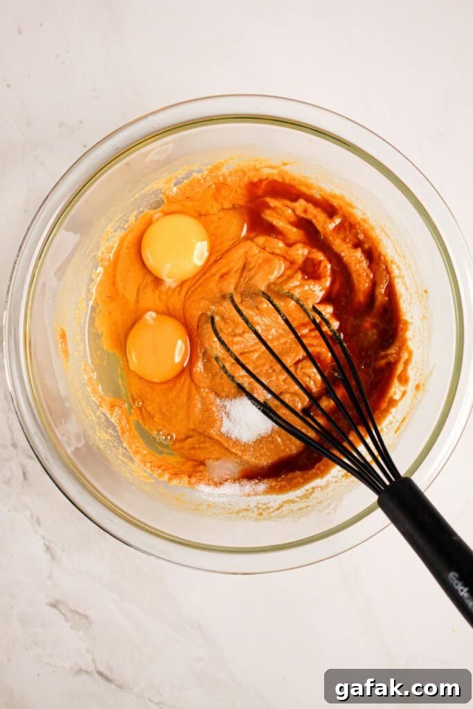 Eggs and vanilla being mixed into batter in a glass mixing bowl. 