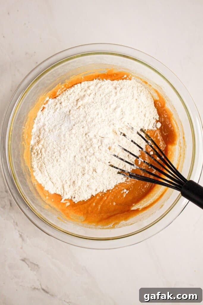 Dry ingredients being added to batter in a glass bowl.