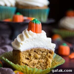 A half eaten pumpkin pie cupcake with cream cheese frosting.