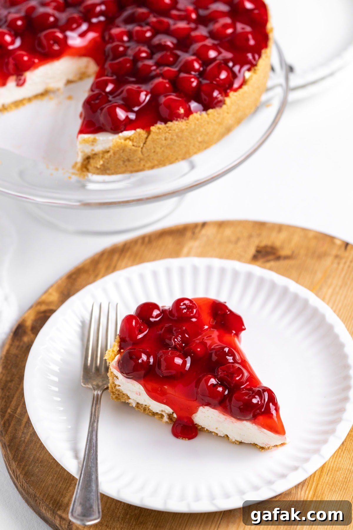 slice of no bake cherry cheesecake on plate with rest of cheesecake in background