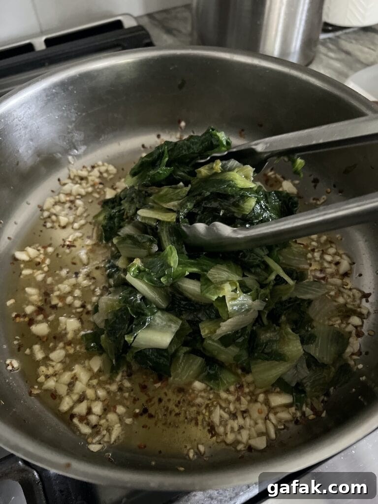 Adding escarole to pan with browned garlic.