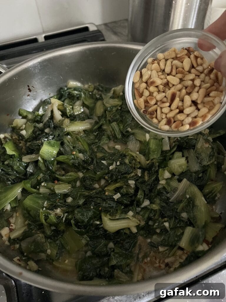 Adding toasted pine nuts to the pan with sautéed vegetables.
