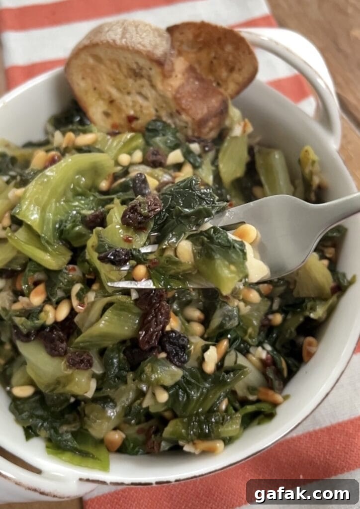 Close up of forkful of sautéed Italian Escarole with pine nuts and raisins with plate of it in background.