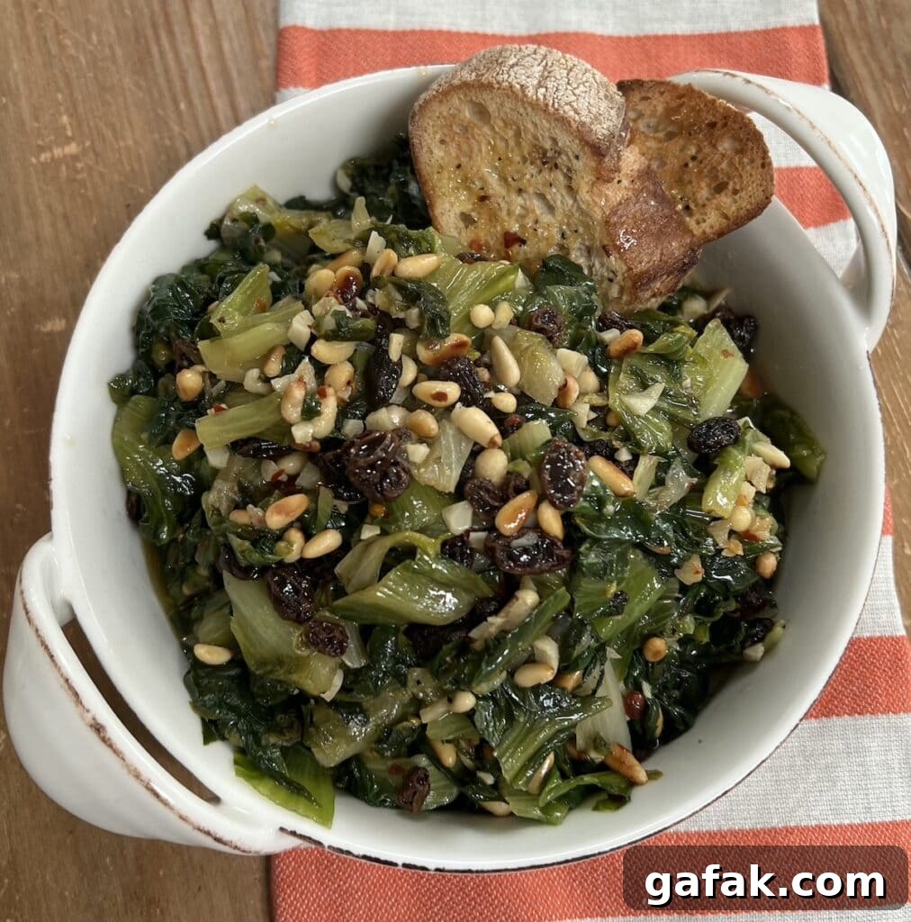 Sautéed Italian Escarole with pine nuts and raisins with 2 slices toasted bread in white dish over decorative towel