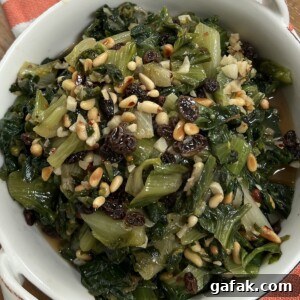 Sautéed Italian Escarole with pine nuts and raisins in white bowl with toasted bread