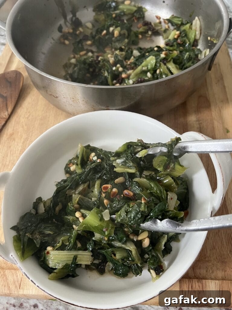 Transferring Sautéed Italian Escarole with pine nuts and raisins from stain steel pan to white dish with tongs.