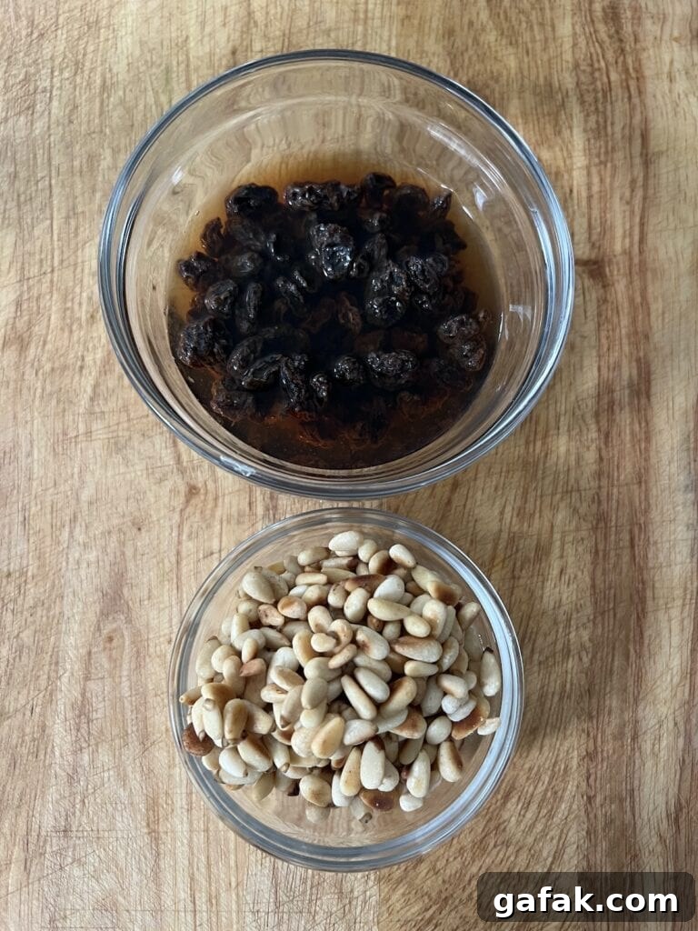 Two small glass bowls with toasted pine nuts and raisins soaking in vinegar.