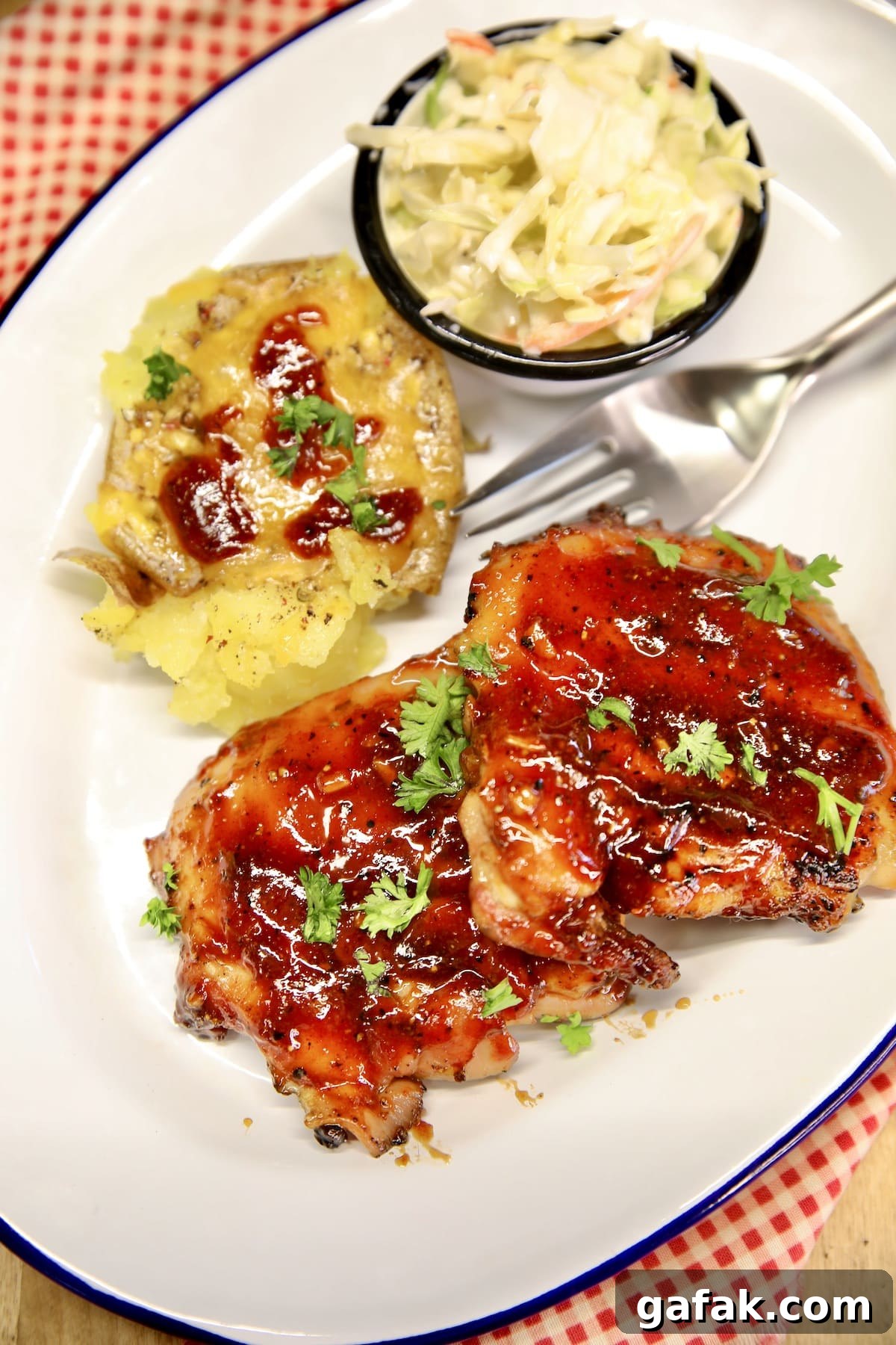 BBQ Chicken thighs on a plate with slaw and potato.