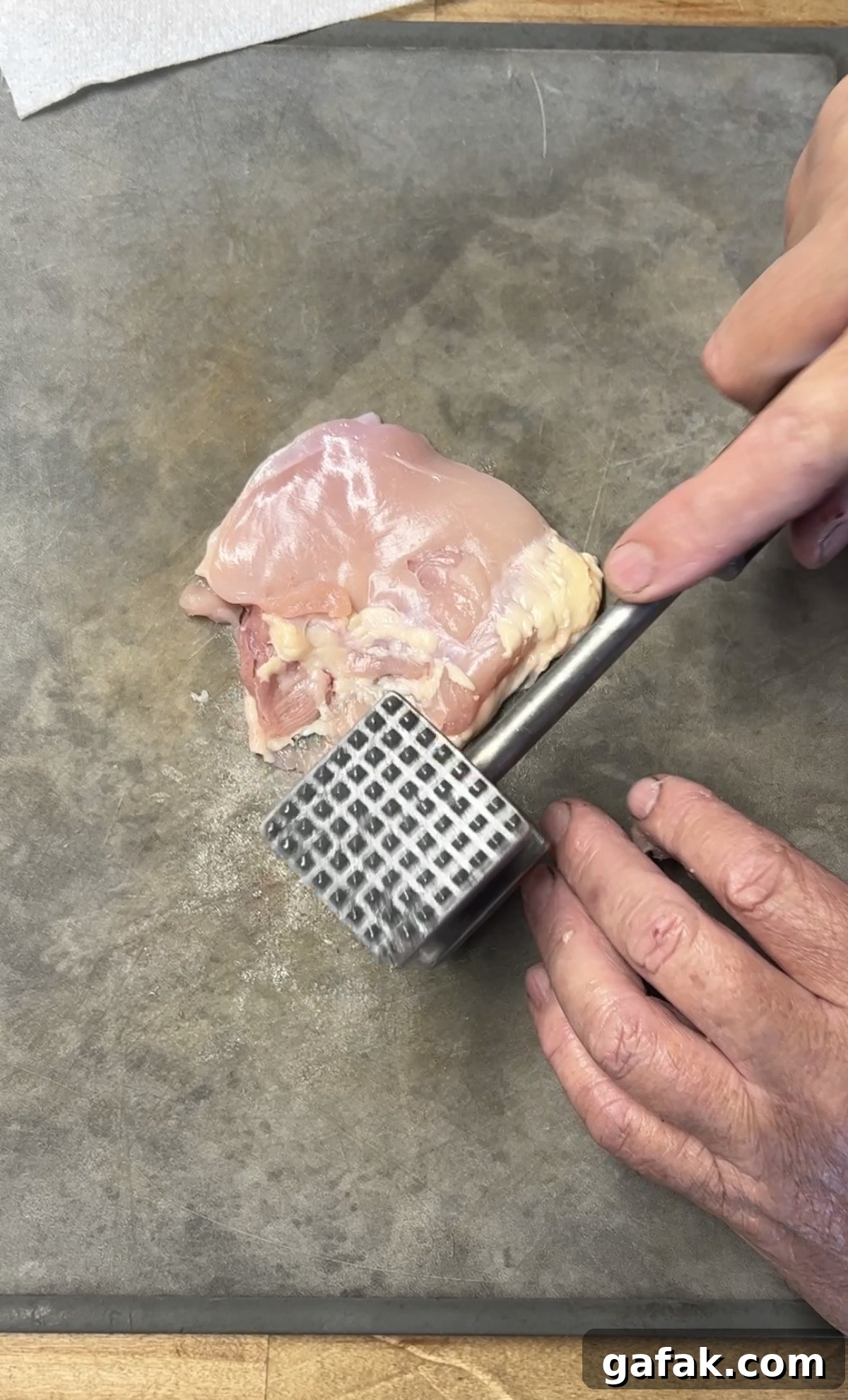 Pounding chicken thighs flat with meat mallet.