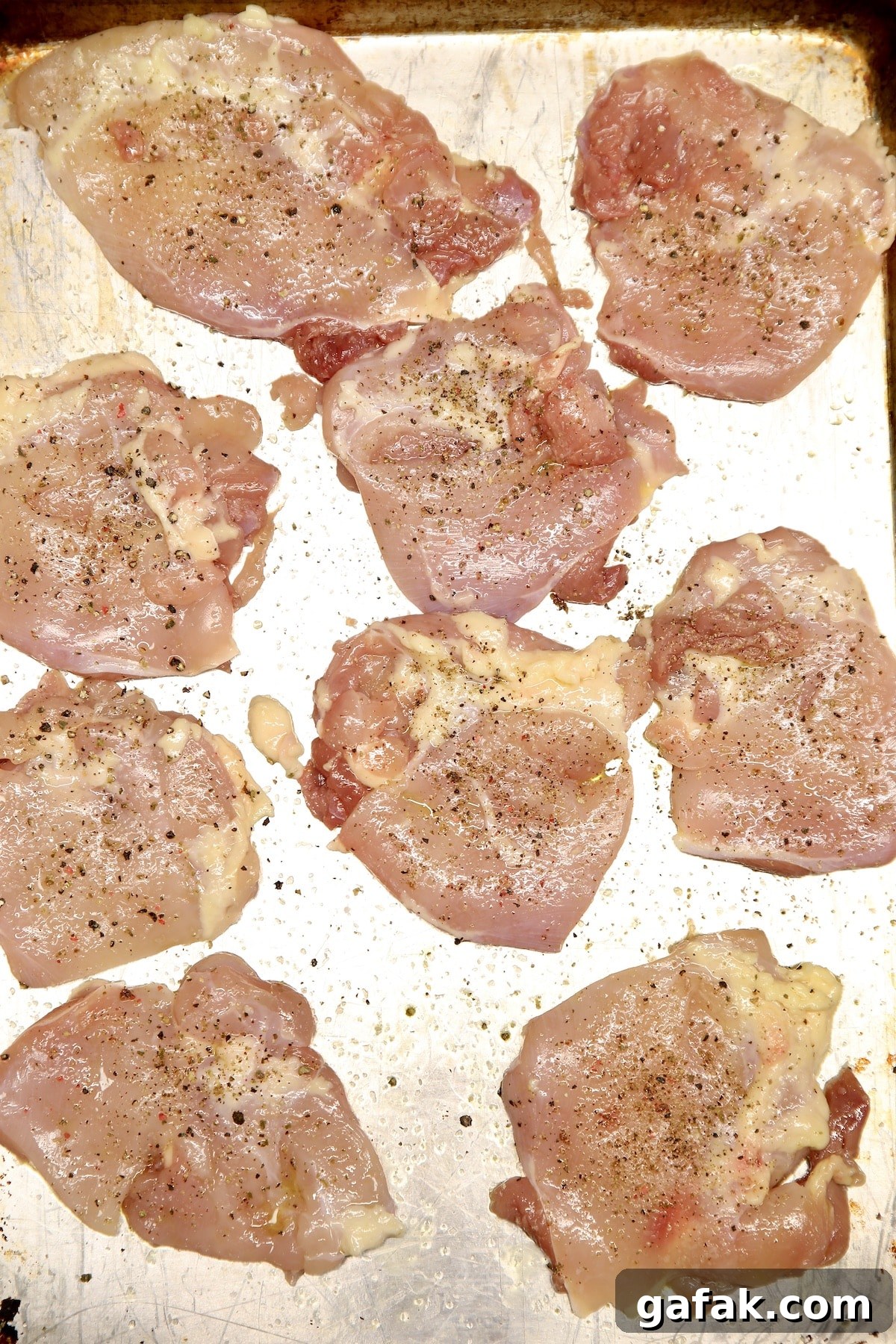 Raw boneless skinless chicken thighs seasoned with salt and pepper on a baking sheet.