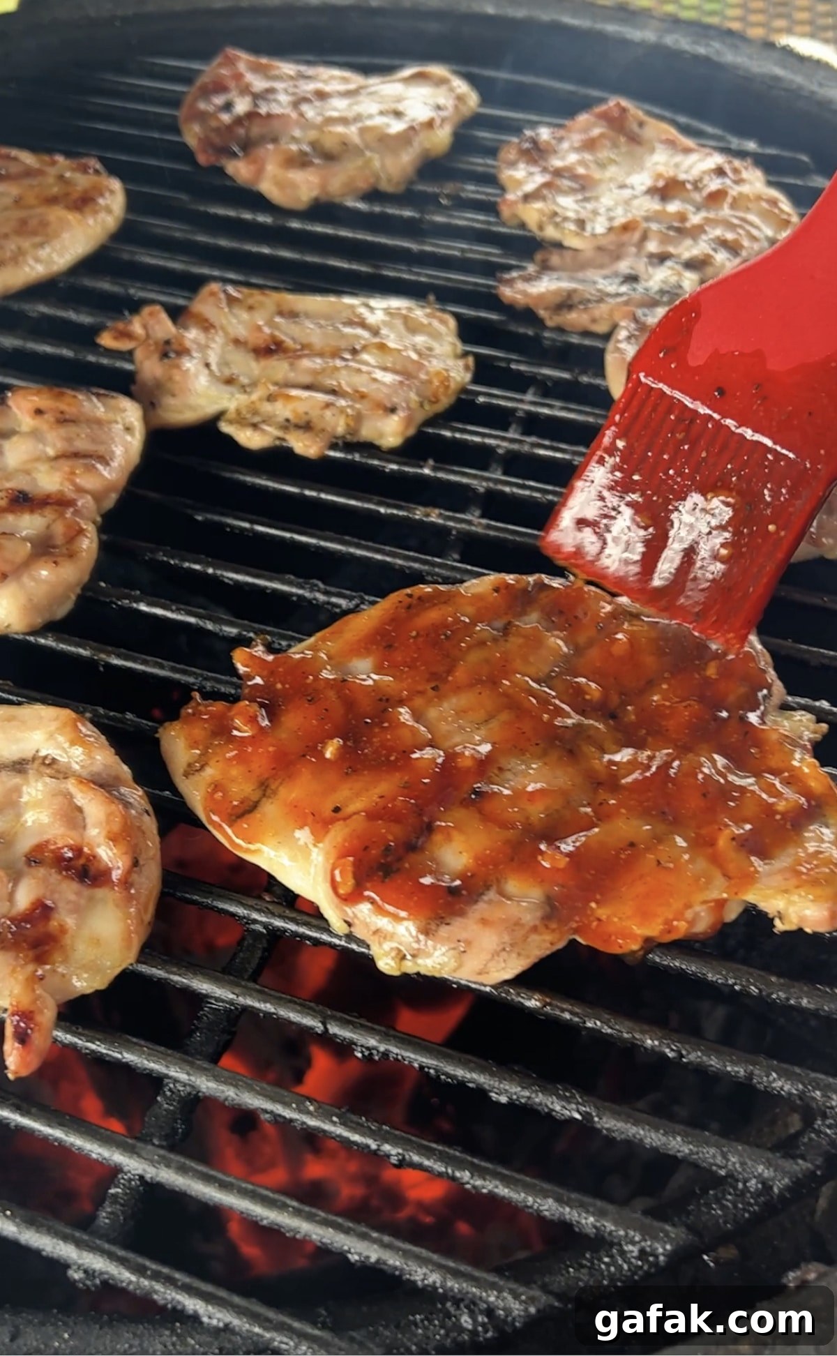 Brushing BBQ sauce onto chicken thighs on grill.