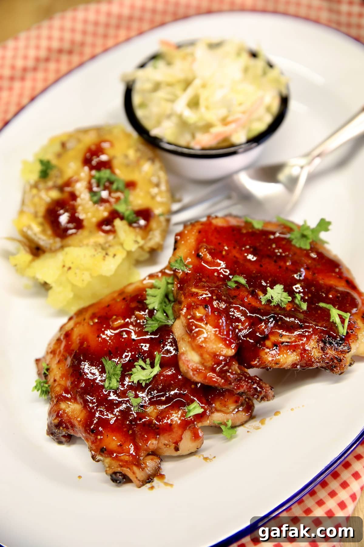2 bbq chicken thighs on a plate with potato and slaw.