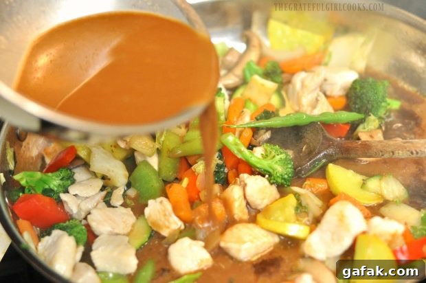An Asian-inspired sauce is added to the skillet full of chicken veggie stir fry.