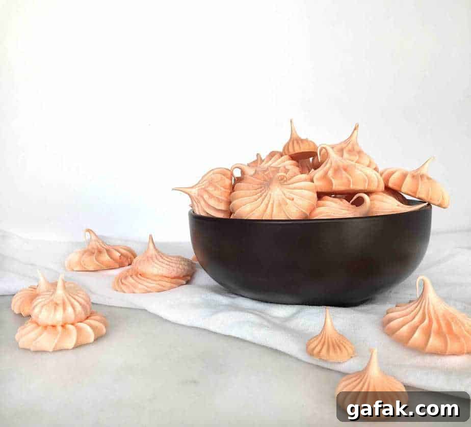 Crisp Pumpkin Spice Meringue Cookies — Light Fall Dessert 3 meringue cookies in a black bowl and spilling out onto a white dish towel