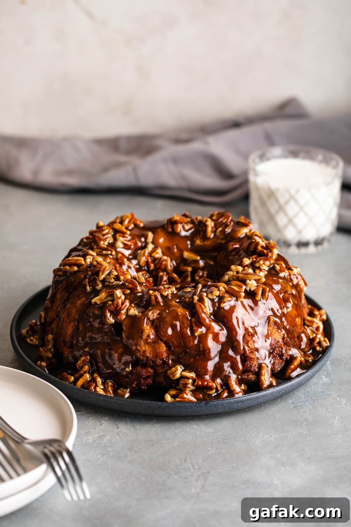 cinnamon roll monkey bread with pecan caramel sauce and a glass of milk in the back