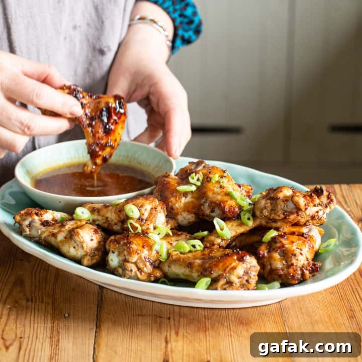 Sticky Honey Chicken Wings Recipe: Crispy Baked or Fried Wings 11 womans hands dipping a golden brown hot chicken wing into a small bowl of hot dipping sauce