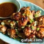 Sticky Honey Chicken Wings Recipe: Crispy Baked or Fried Wings 12 pale blue plate of crispy brown chicken wings with a small bowl of brown dipping sauce