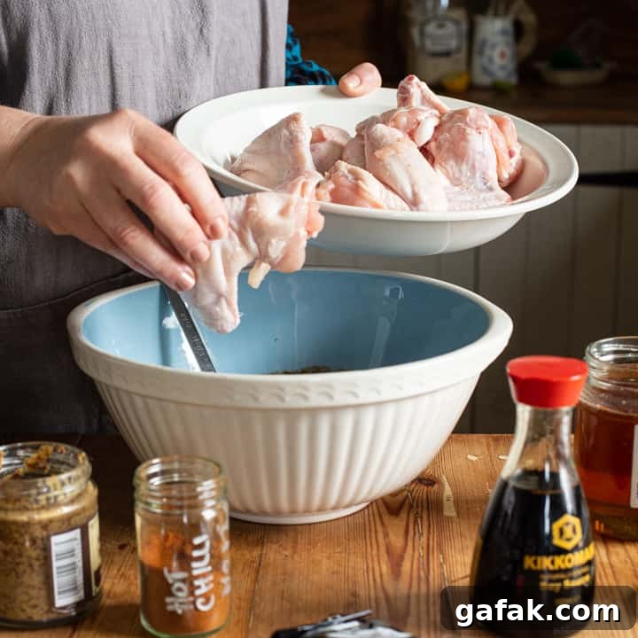 Sticky Honey Chicken Wings Recipe: Crispy Baked or Fried Wings 5 woman in grey moving raw chicken wings from a large white plate into a pale blue mixing bowl