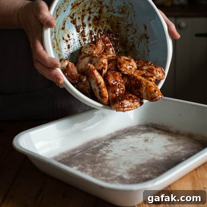 Sticky Honey Chicken Wings Recipe: Crispy Baked or Fried Wings 7 womans hands tipping a bowl of marinated chicken wings into an old white enamel baking tray