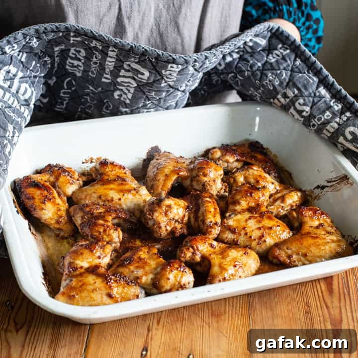 Sticky Honey Chicken Wings Recipe: Crispy Baked or Fried Wings 8 womans hands in black and white oven gloves holding a hot tray of sticky chicken wings