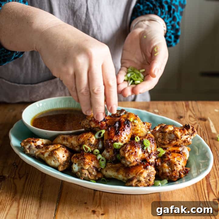 Sticky Honey Chicken Wings Recipe: Crispy Baked or Fried Wings 10 womans hands sprinkling green spring onion over a blue plate of chicken wings