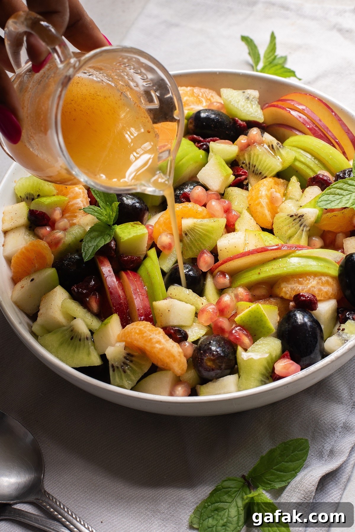 Salad with dressing being poured onto it from a jug.