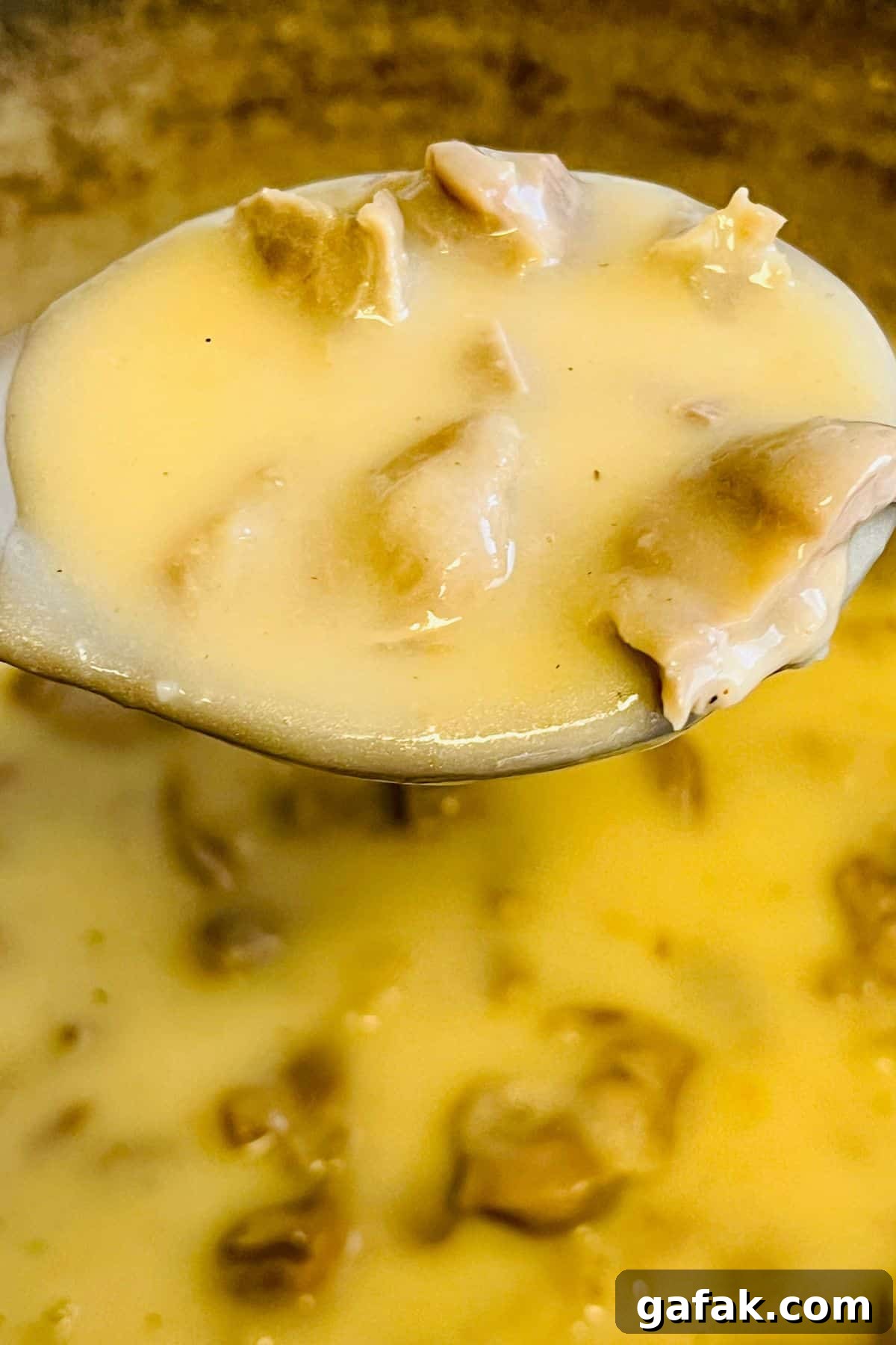 A close-up of a ladle holding creamy Turkey Neck Gravy with chunks of chicken, suspended over a pot filled with more savory gravy.
