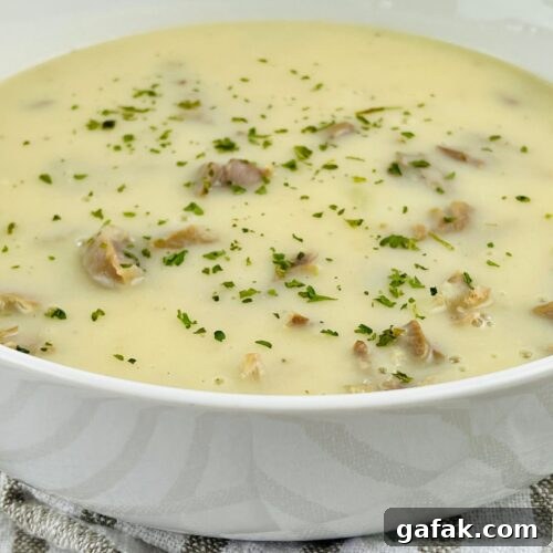 A bowl of creamy soup with visible mushroom pieces, garnished with chopped herbs and a hint of savory Turkey Neck Gravy, placed on a striped cloth.