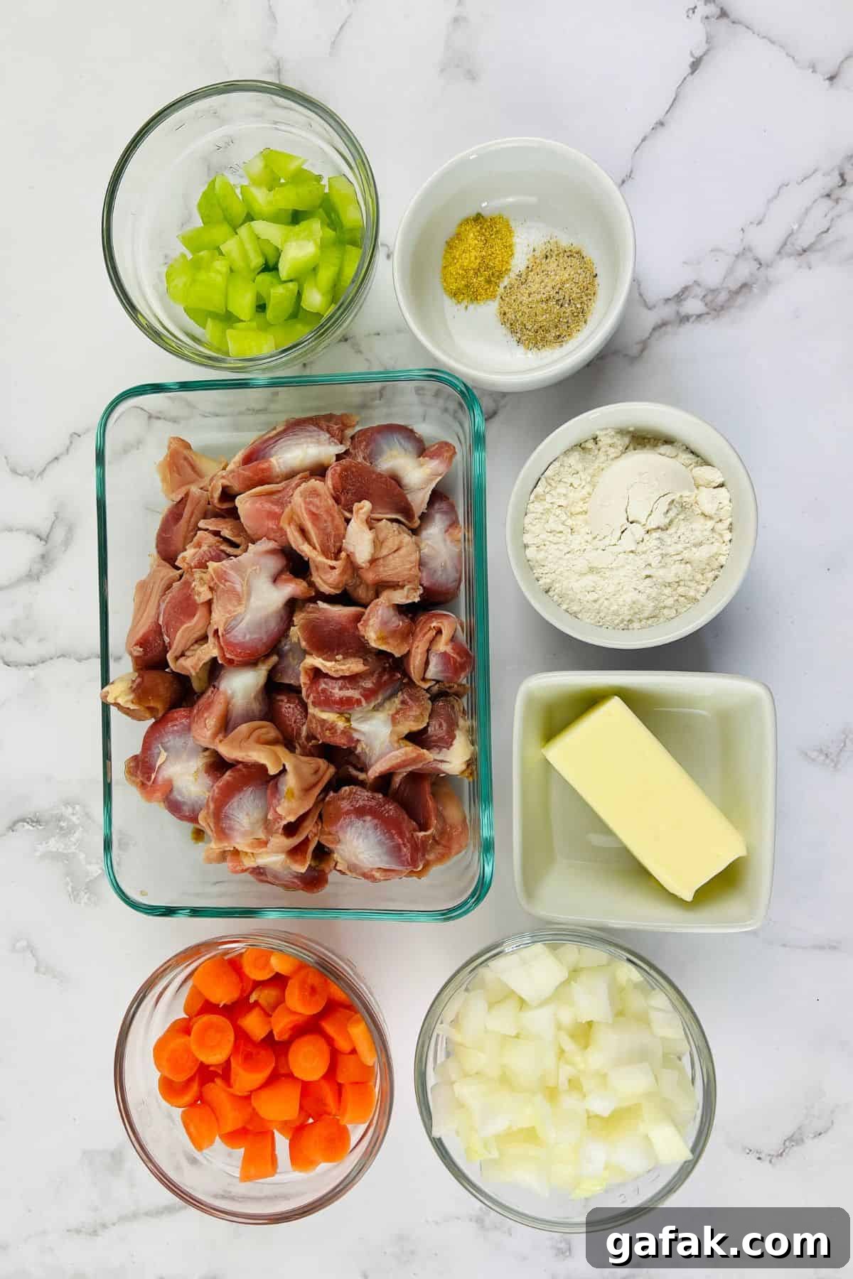 Overhead view of chopped raw turkey gizzards, diced celery, carrots, onions, flour, butter, and seasoning in separate bowls on a marble surface—ingredients perfect for starting classic Turkey Neck Gravy.