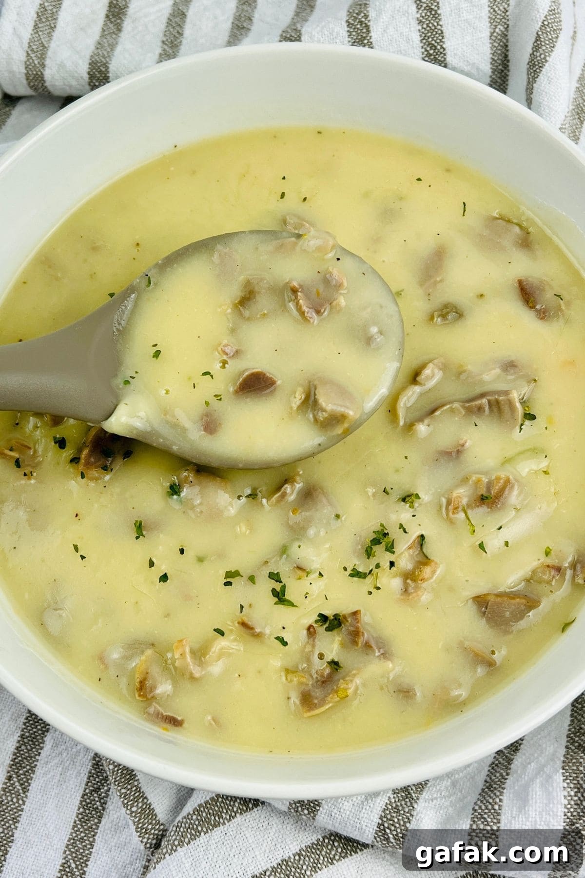 A bowl of creamy soup with chunks of mushrooms, finished with herbs and a hint of rich Turkey Neck Gravy, with a spoon resting inside the bowl.
