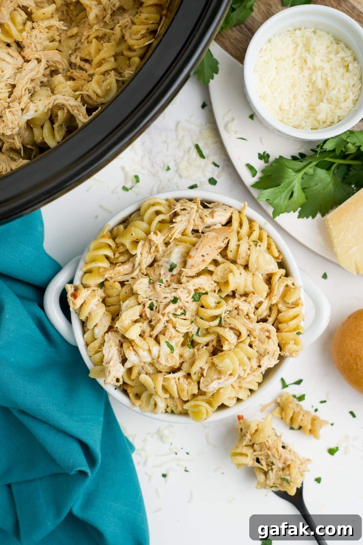 Garlic Parmesan Chicken Pasta in the Crockpot — Creamy Slow-Cooker Recipe 2 A bowl of crockpot garlic parmesan chicken on a table with a slow cooker in the corner.