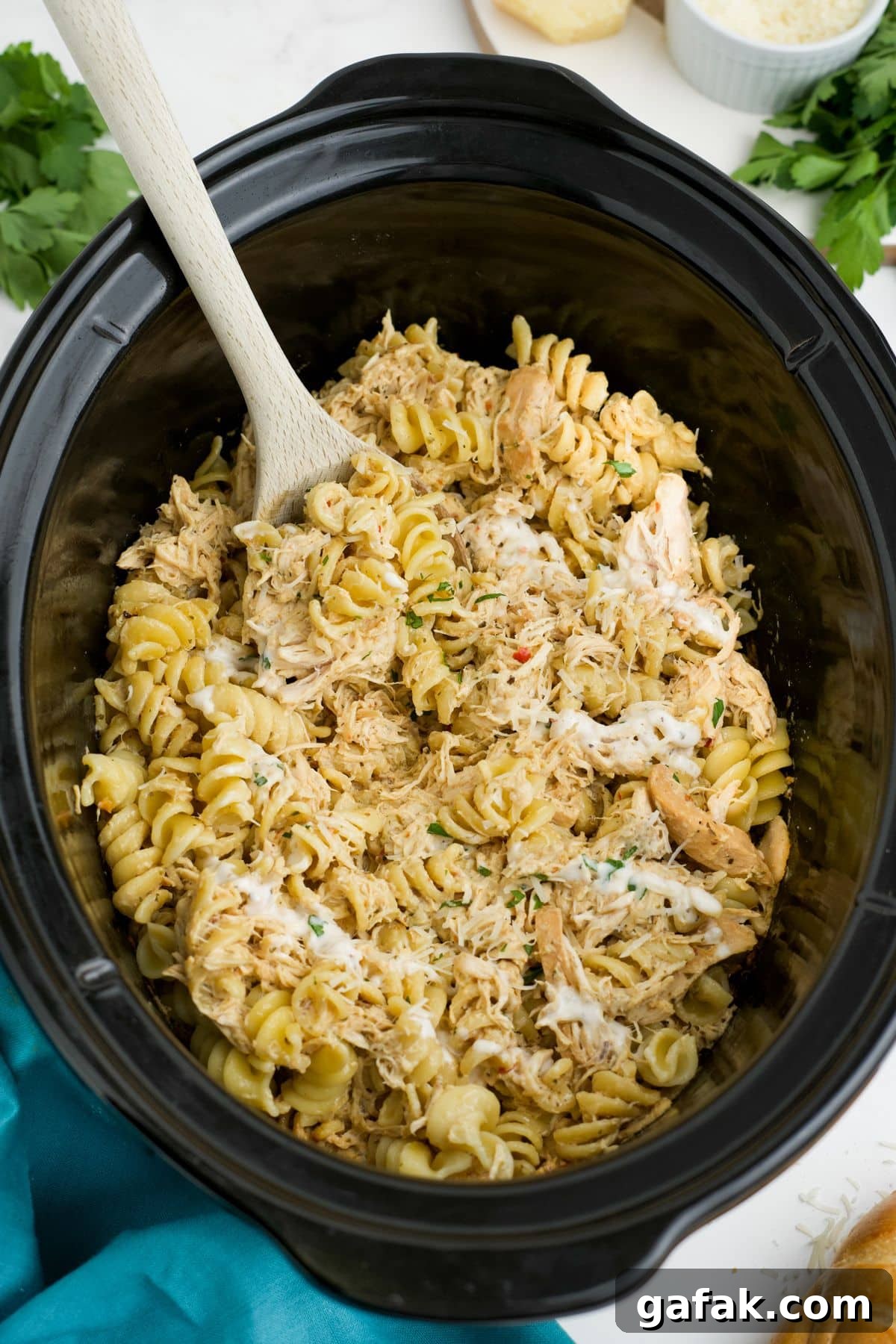 Garlic Parmesan Chicken Pasta in the Crockpot — Creamy Slow-Cooker Recipe 10 Garlic parmesan chicken and pasta in a slow cooker with a wooden spoon resting on the side.