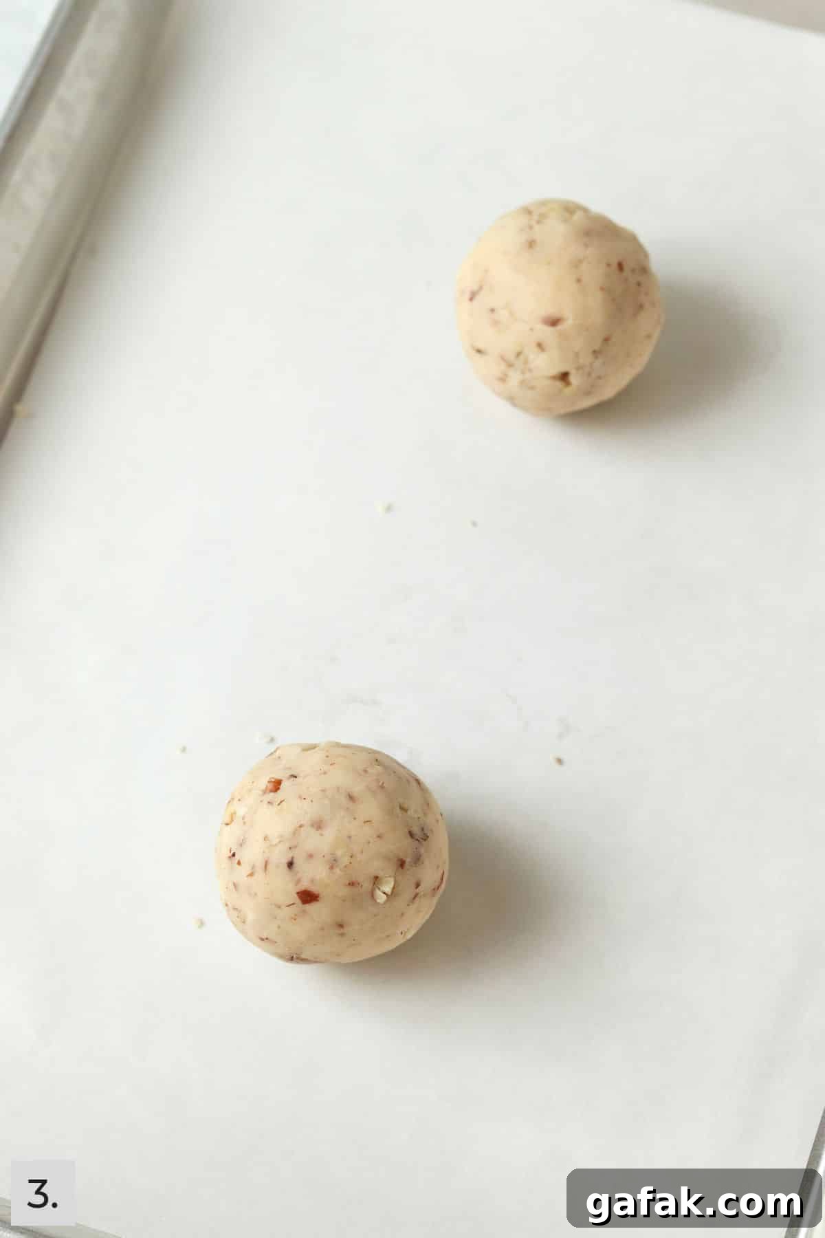 Two snowball cookie dough balls unbaked on a cookie sheet.