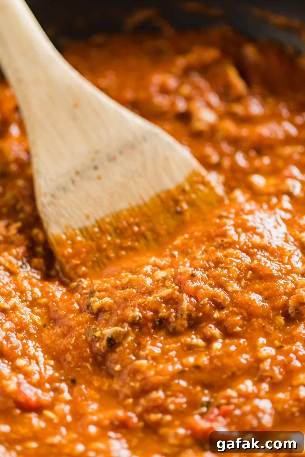 A close up of a wooden spoon stirring red clam sauce.