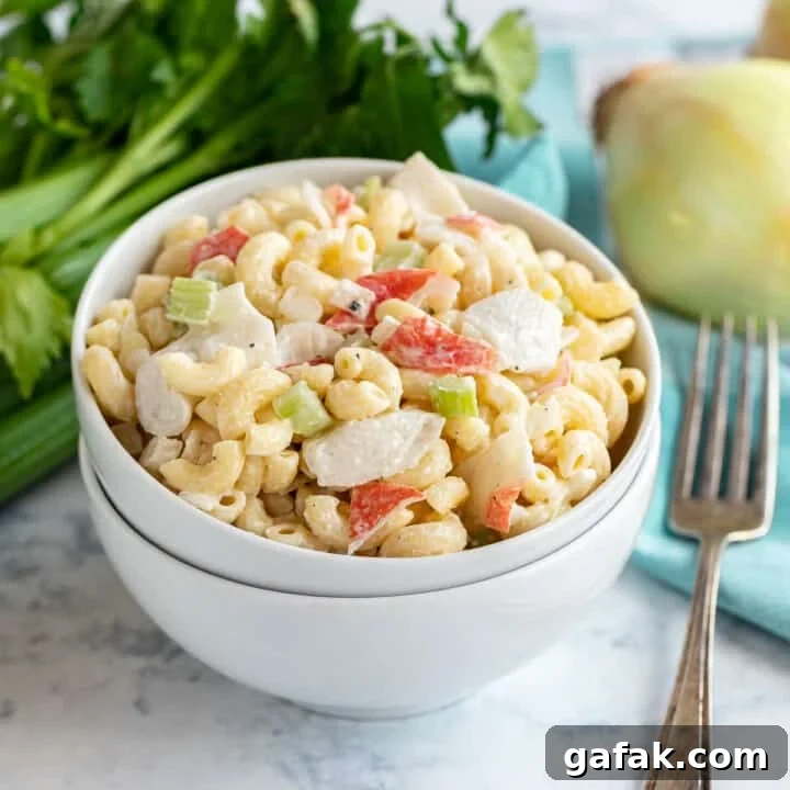 A bowl of crab mac salad on top of a second bowl with celery and an onion behind it.
