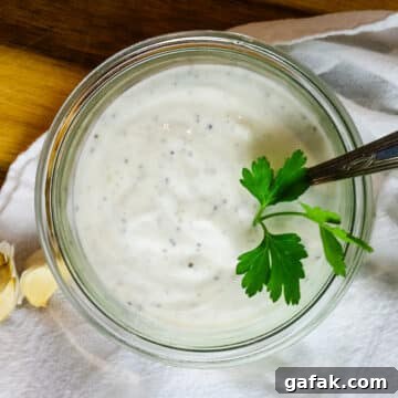 garlic sauce with specks of black pepper and minced garlic with fresh parsley leaf.