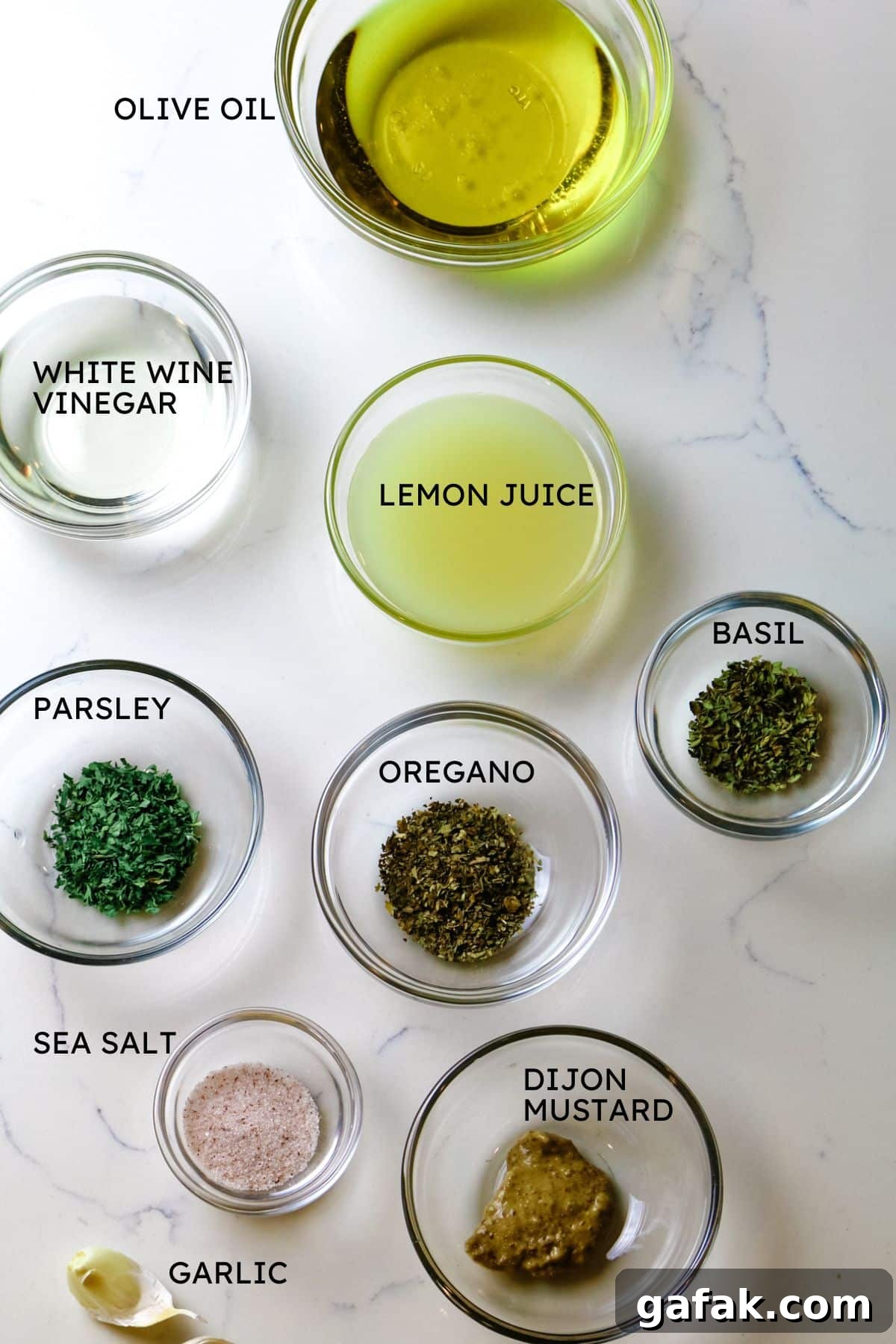 ingredients for salad dressing with olive oil, white wine vinegar, lemon juice, herbs, and Dijon mustard.