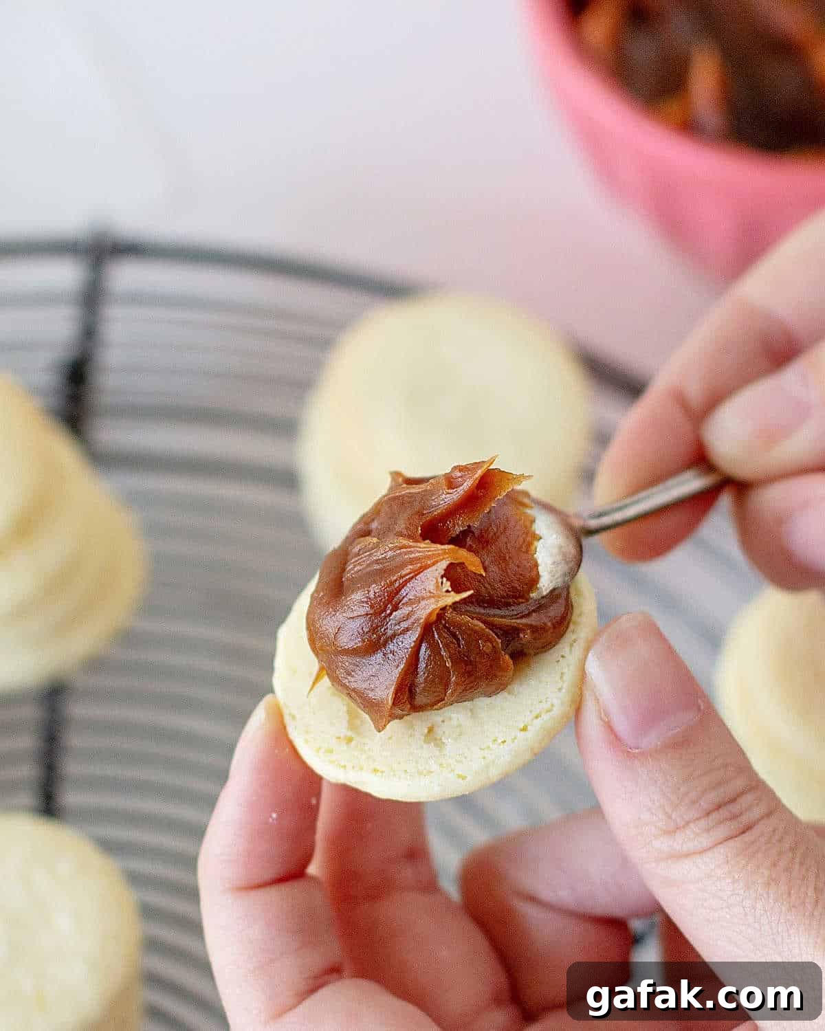 Placing a teaspoon of dulce de leche on a cornstarch cookie. More cookies on a wire rack below.