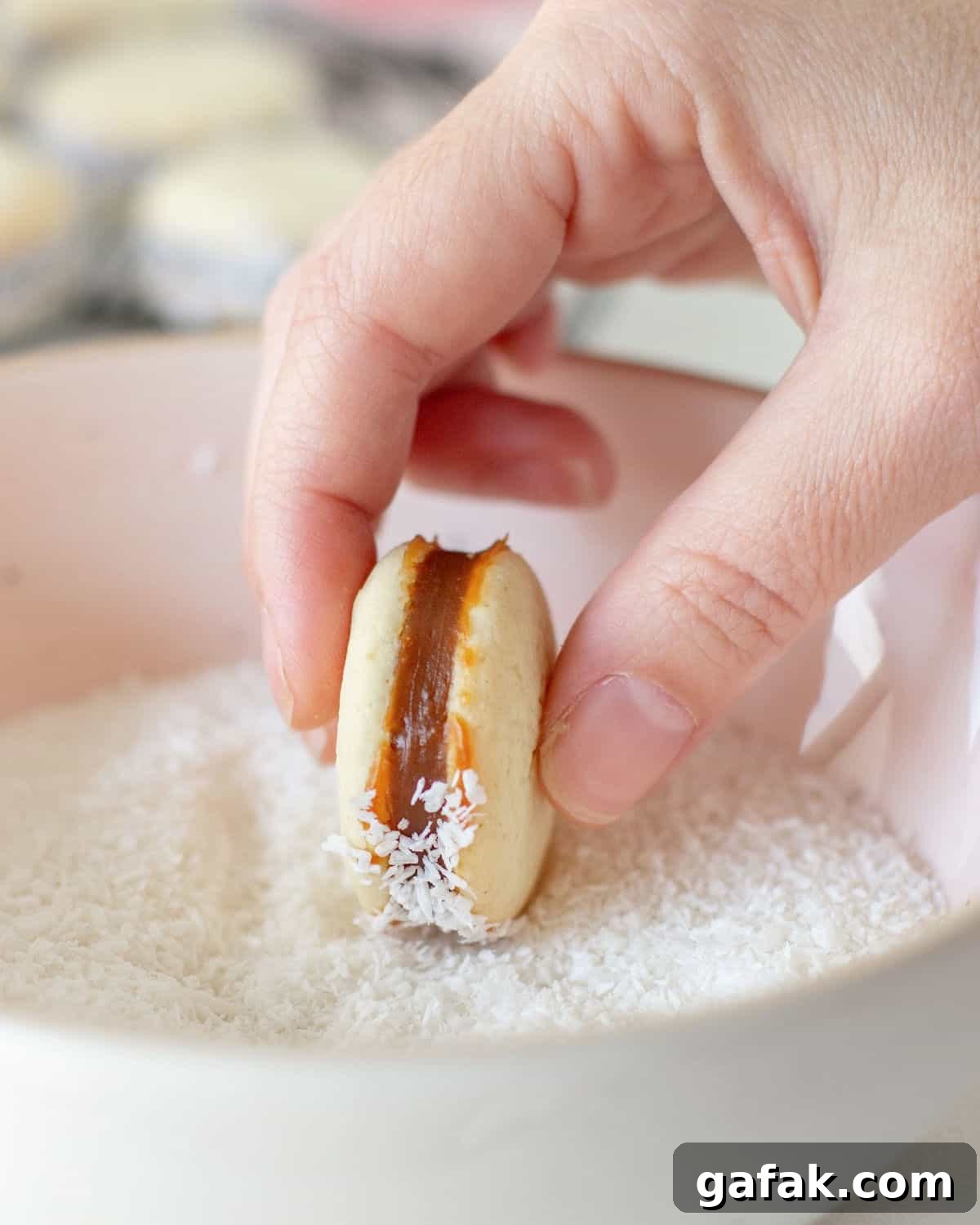 Rolling a cornstarch alfajor in shredded coconut placed in a pink bowl.