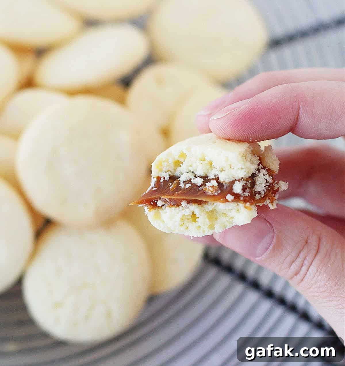 Hand holding half eaten alfajor; loose cookies in background