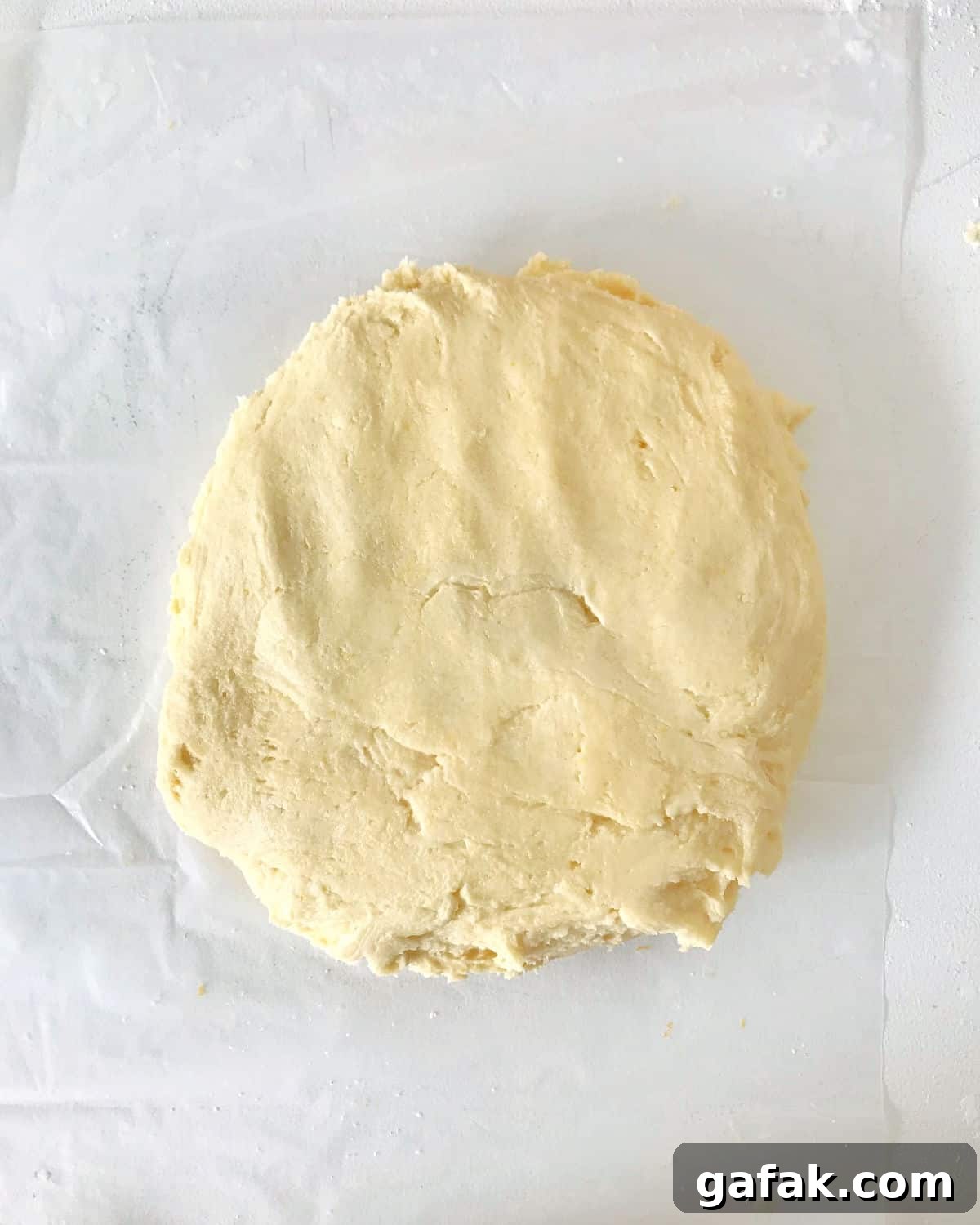 Round disc of vanilla dough on a transparent sheet of paper on a white surface.