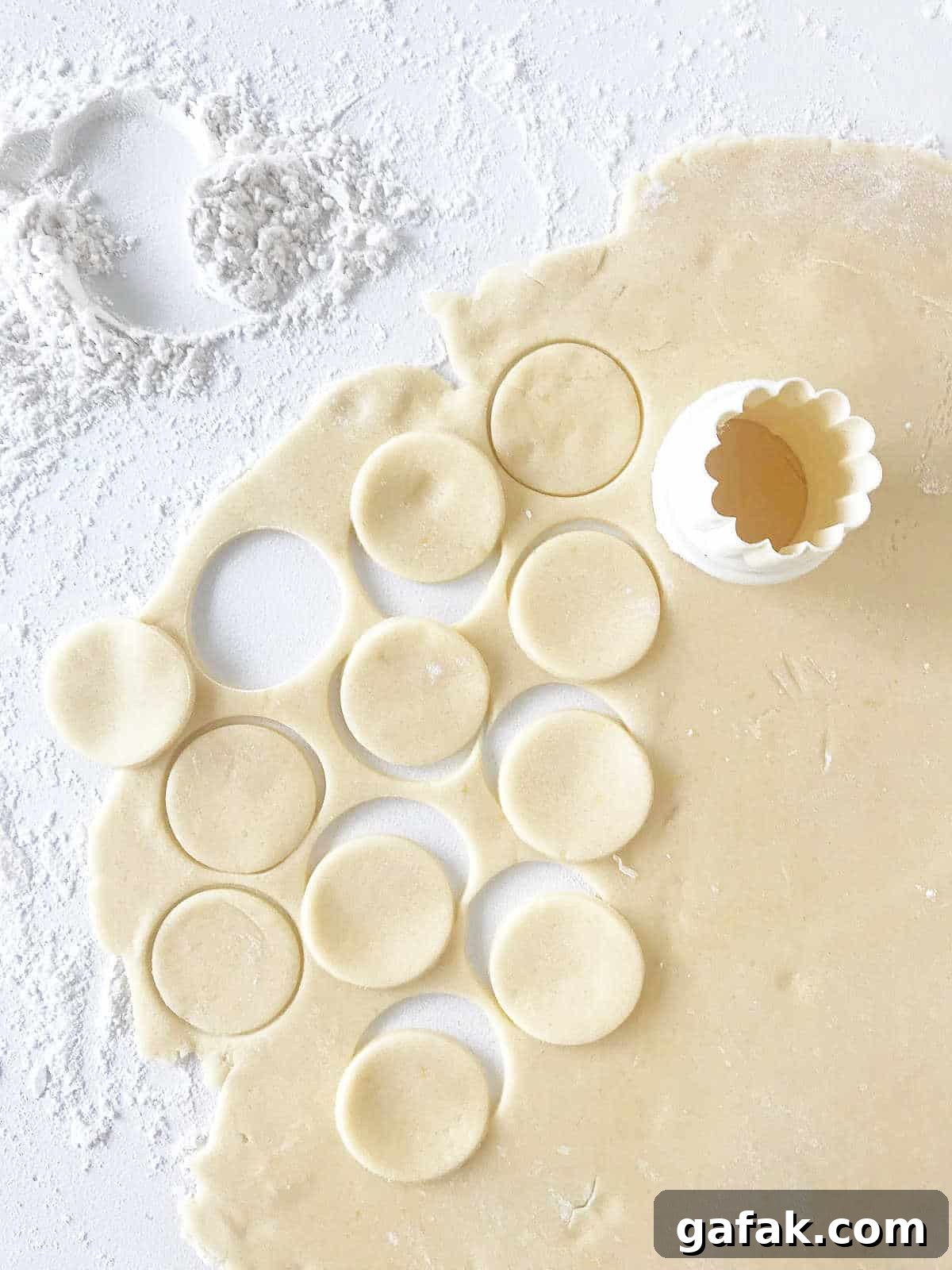 Rolled cookie dough on a floured white surface with round cutter and some cut circles of dough.