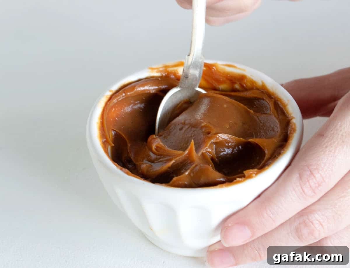 Hand dipping spoon in white bowl of dulce de leche.