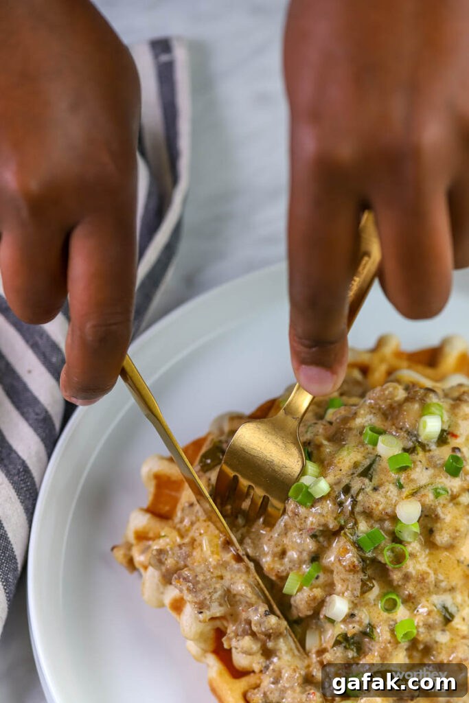 hands cutting into waffles with sausage gravy