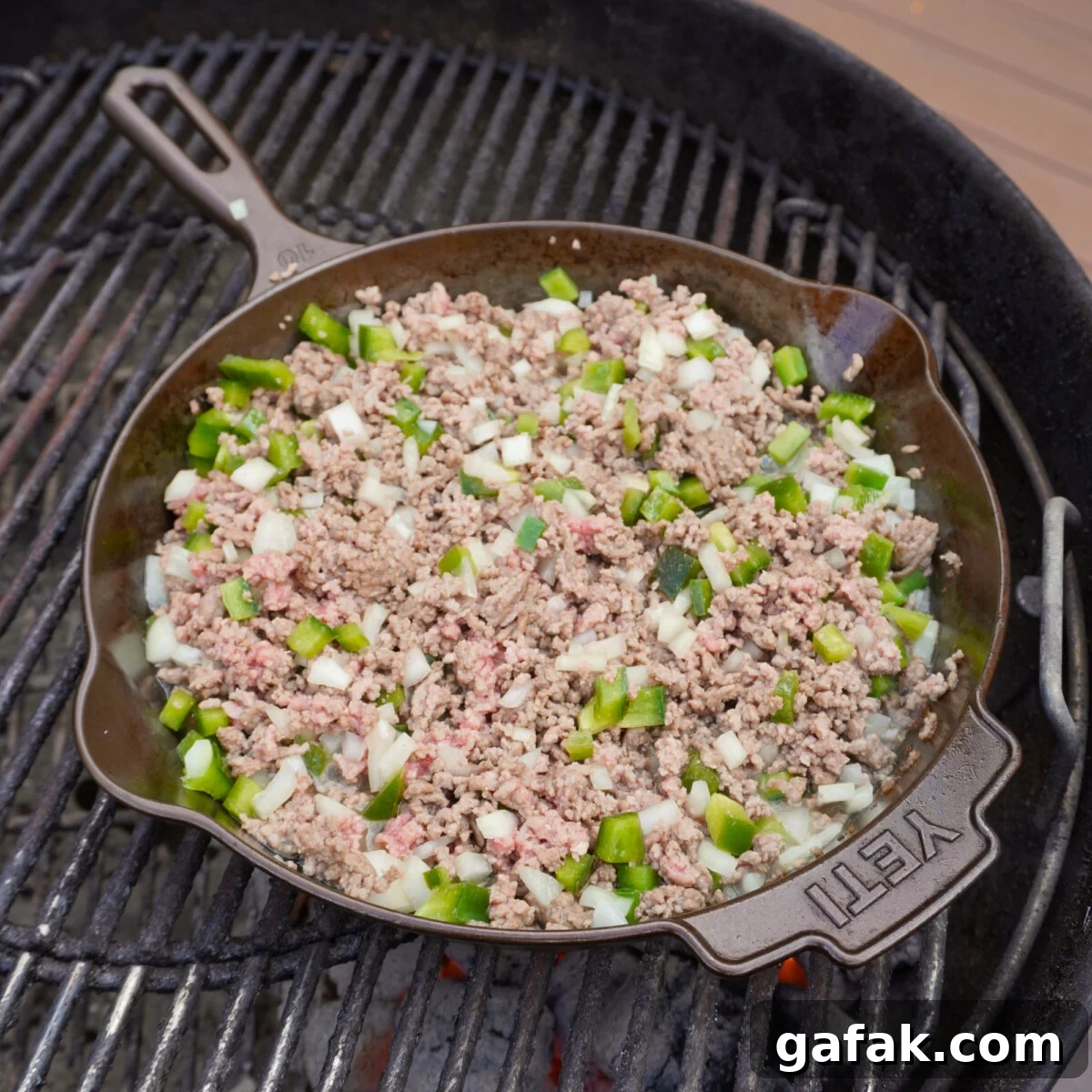 a cast iron skillet on the grill with cooked ground beef and chopped veggies.
